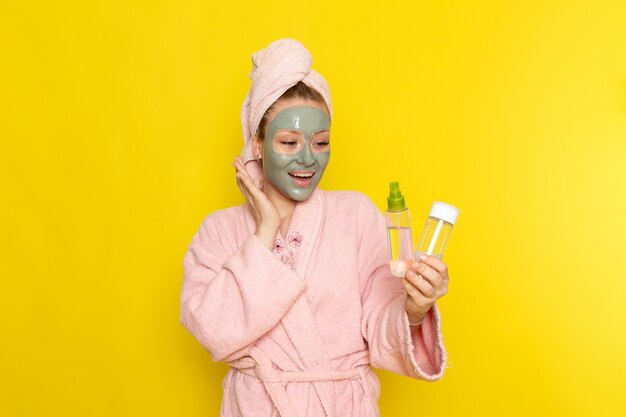 Een vooraanzicht jonge mooie vrouw in roze badjas bedrijf sprays glimlachen