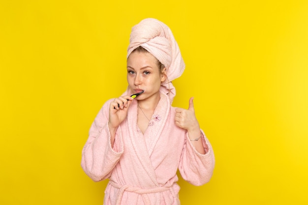 Een vooraanzicht jonge mooie vrouw in roze badjas haar tanden poetsen