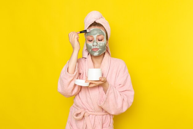 Een vooraanzicht jonge mooie vrouw in roze badjas make-up doen