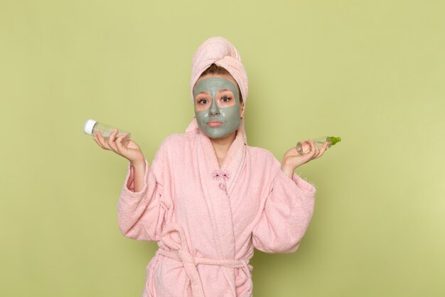 Een vooraanzicht jonge mooie vrouw in roze badjas met gezichtsmasker met sprays