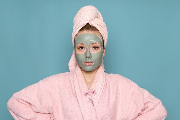Een vooraanzicht jonge mooie vrouw in roze badjas met gezichtsmasker
