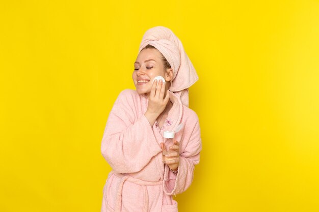 Een vooraanzicht jonge mooie vrouw in roze badjas opruimen alle make-up met een glimlach