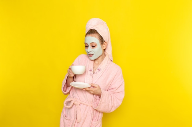 Een vooraanzicht jonge mooie vrouw in roze badjas thee drinken