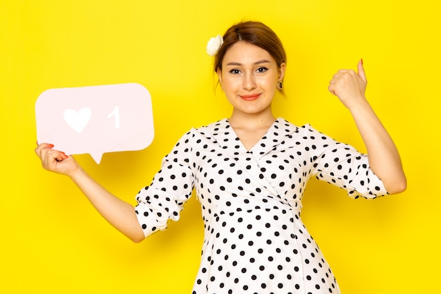 Een vooraanzicht jonge mooie vrouw in zwart-witte polka dot jurk met wit als teken en lachend op geel