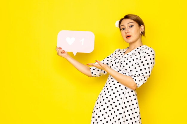 Een vooraanzicht jonge mooie vrouw in zwart-witte polka dot jurk met wit als teken op geel