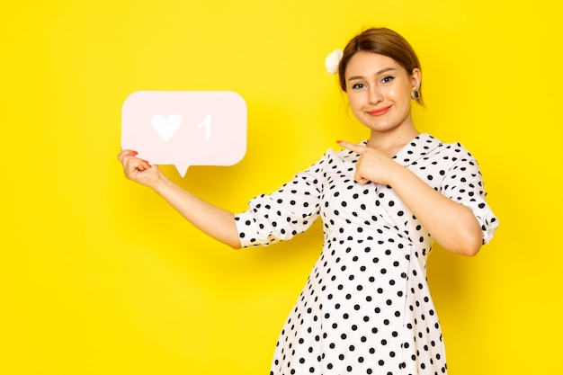 Een vooraanzicht jonge mooie vrouw in zwart-witte polka dot jurk met wit als teken op geel