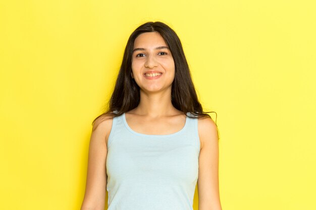 Een vooraanzicht jonge vrouw in blauw shirt lachend op de gele achtergrond meisje stelt model schoonheid jong
