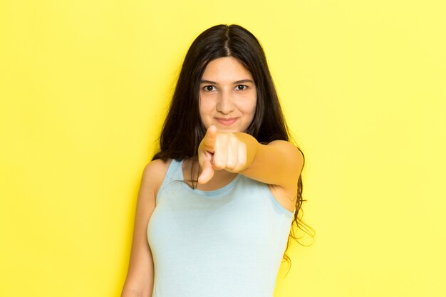 Een vooraanzicht jonge vrouw in blauw shirt poseren en lachend met puntige vinger op de gele achtergrond meisje pose model schoonheid jong