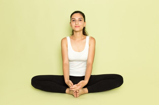 Een vooraanzicht jonge vrouw in wit overhemd en zwarte broek poseren zittend in mediterende yoga pose