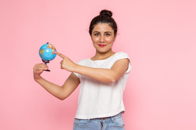 Een vooraanzicht jonge vrouw in wit t-shirt en spijkerbroek met kleine wereldbol