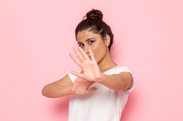 Een vooraanzicht jonge vrouw in wit t-shirt en spijkerbroek poseren met haar handen