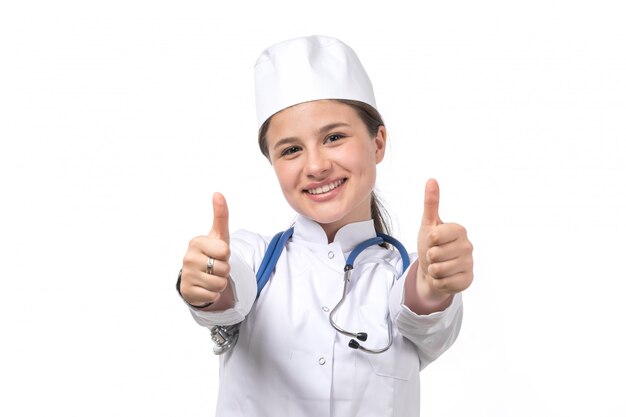 Een vooraanzicht jonge vrouwelijke arts in witte medische pak en witte dop met blauwe stethoscoop glimlachen