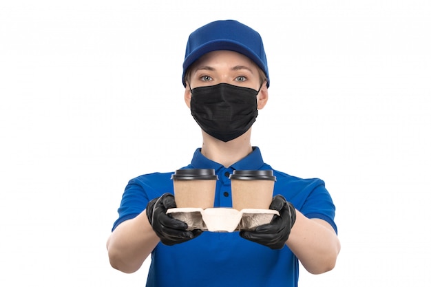 Een vooraanzicht jonge vrouwelijke koerier in blauw uniform zwart masker en handschoenen met koffiekopjes