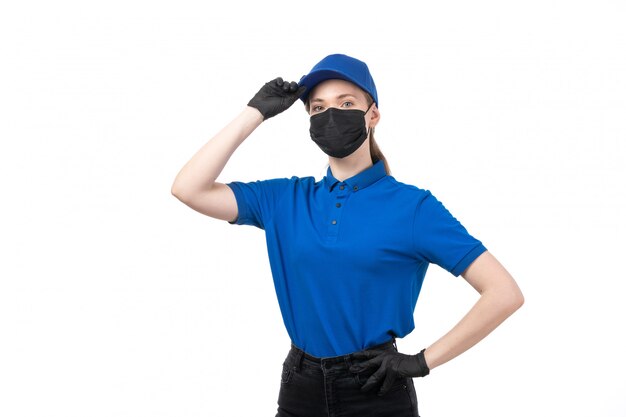 Een vooraanzicht jonge vrouwelijke koerier in blauwe uniforme zwarte handschoenen en zwart masker poseren