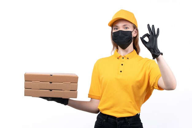 Een vooraanzicht jonge vrouwelijke koerier in gele uniforme zwarte handschoenen en zwart masker met pizzadozen