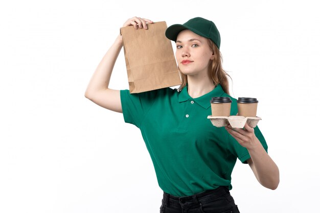 Een vooraanzicht jonge vrouwelijke koerier in groen uniform glimlachend bedrijf voedselpakket en koffiekopjes