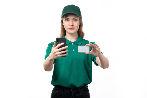 Een vooraanzicht jonge vrouwelijke koerier in groen uniform glimlachend bedrijf witte kaart en smartphone