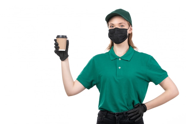 Een vooraanzicht jonge vrouwelijke koerier in groene uniforme zwarte handschoenen en zwart masker met koffiekopje