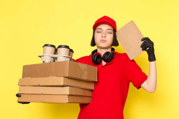 Een vooraanzicht jonge vrouwelijke koerier in rode uniforme zwarte handschoenen en rode dop met voedseldozen en koffiekopjes