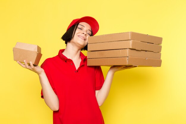 Een vooraanzicht jonge vrouwelijke koerier in rode uniforme zwarte handschoenen en rode dop met voedseldozen