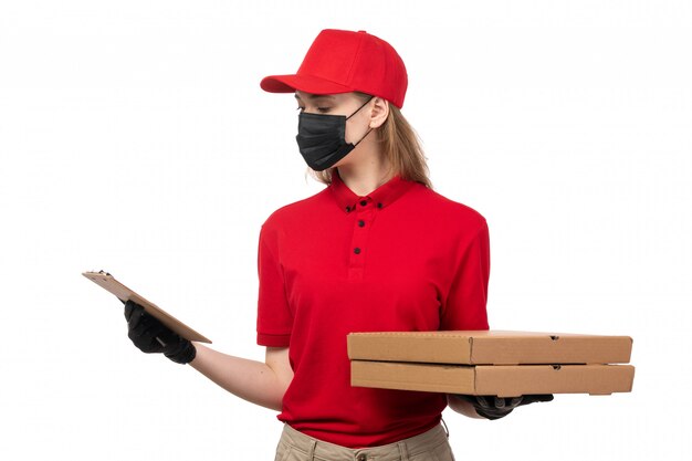 Een vooraanzicht jonge vrouwelijke koerier in rood overhemd, rode pet, zwarte handschoenen en zwart masker met pizzadozen service