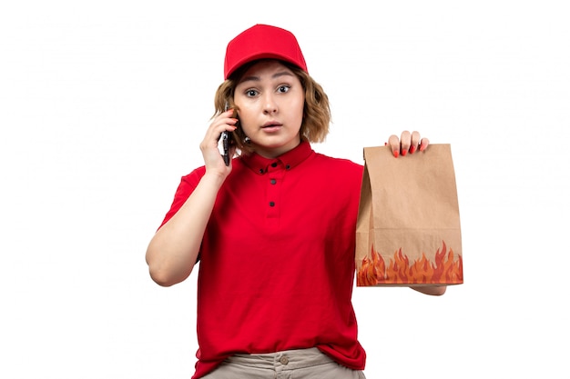 Een vooraanzicht jonge vrouwelijke koerier in rood shirt, rode pet, bedrijf levering voedselpakket praten aan de telefoon