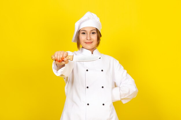Een vooraanzicht jonge vrouwelijke kok in wit kokkostuum en wit GLB-holdingsmes die op het geel glimlachen