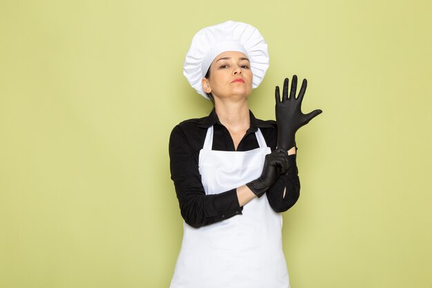 Een vooraanzicht jonge vrouwelijke kok in zwarte shirt witte kok cape witte dop poseren zwarte handschoenen poseren