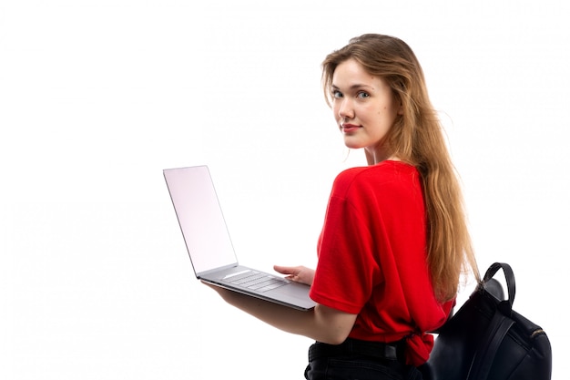 Gratis foto een vooraanzicht jonge vrouwelijke student in rode overhemd zwarte zak die laptop op het wit met behulp van