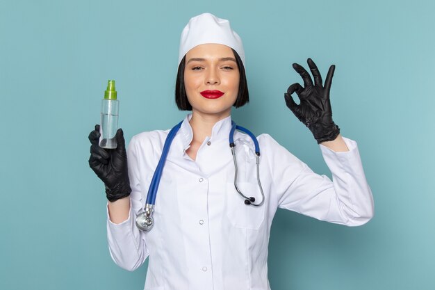 Een vooraanzicht jonge vrouwelijke verpleegster in wit medisch pak en blauwe stethoscoop met spray op de blauwe bureau geneeskunde ziekenhuis arts
