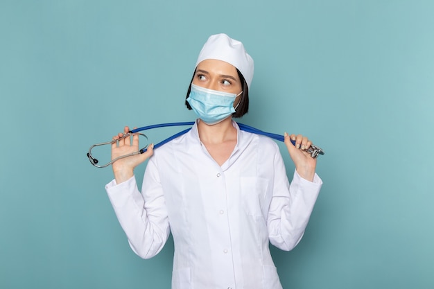Gratis foto een vooraanzicht jonge vrouwelijke verpleegster in wit medisch pak en blauwe stethoscoop poseren op de blauwe bureau geneeskunde ziekenhuis arts