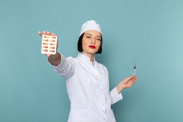 Een vooraanzicht jonge vrouwelijke verpleegster in wit medisch pak met pillen op de blauwe bureau geneeskunde ziekenhuis arts