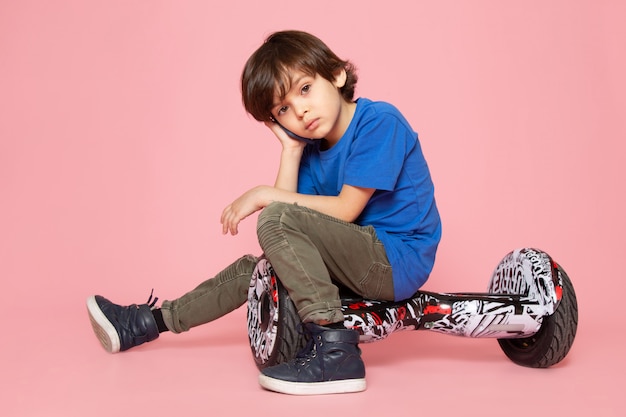 Een vooraanzicht klein kind in blauw t-shirt en kaki broek Segway rijden op de roze ruimte