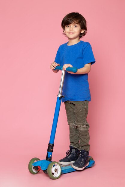 Een vooraanzicht klein kind in blauw t-shirt rijden scooter op de roze vloer