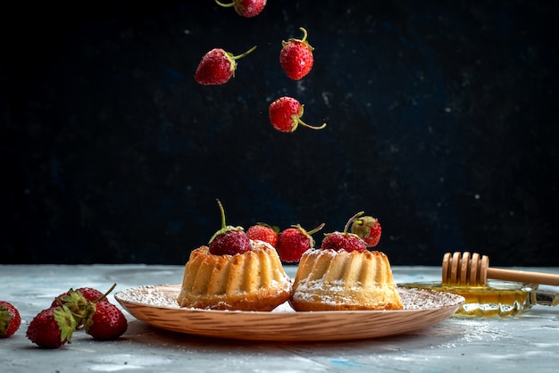 Een vooraanzicht kleine cakes binnen plaat die aardbeien op het lichte koekje van de bureaucake krijgen