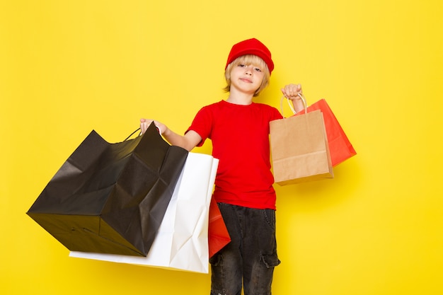 Een vooraanzicht kleine schattige koerier in rode t-shirt rode caps jeans poseren met kleurrijke boodschappenpakketten