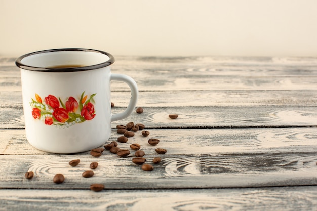 Gratis foto een vooraanzicht kopje koffie met bruine koffiezaden op het grijze rustieke bureau drinkt koffiekleur