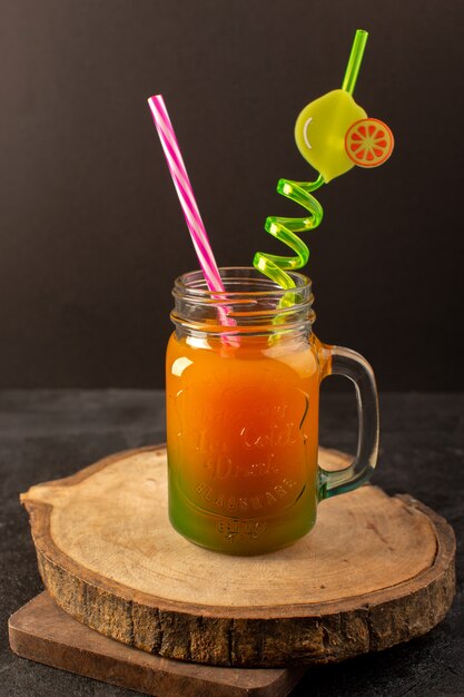 Een vooraanzicht koude cocktail gekleurde binnenkant glas kan met kleurrijke stro geïsoleerd op het houten bureau en donker