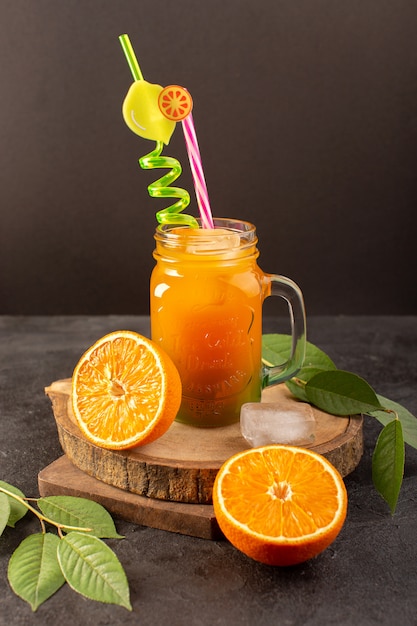 Een vooraanzicht koude cocktail gekleurde binnenkant glas kan met kleurrijke stro met ijsblokjes sinaasappelen en groene bladeren geïsoleerd op het houten bureau en donker