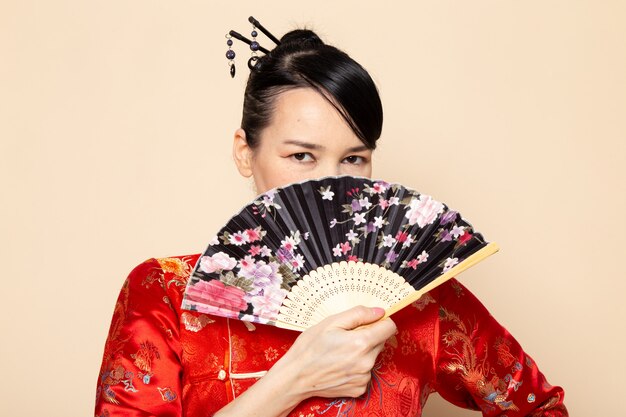 Een vooraanzicht mooie Japanse geisha in traditionele rode Japanse kleding met haar plakt stellende holdings vouwende ventilator elegant op de room achtergrondceremonie Japan