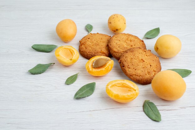 Een vooraanzicht oranje abrikozen geheel en op smaak gebracht met groene bladeren en koekjes op de lichttafel