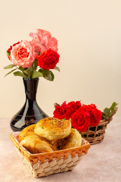 Een vooraanzicht rode rozen mooi roze en bloemen in zwarte kruik samen met qogals in broodtrommel geïsoleerd op tafel en roze