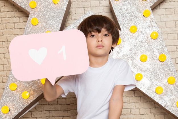 Een vooraanzicht schattige kleine jongen in witte t-shirt donkere jeans op de ster ontworpen gele standaard en lichte achtergrond