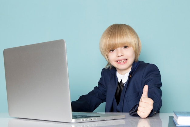 Een vooraanzicht schattige zakelijke jongen in blauwe klassieke pak poseren voor zilveren laptop werken glimlachend zakelijke werk mode