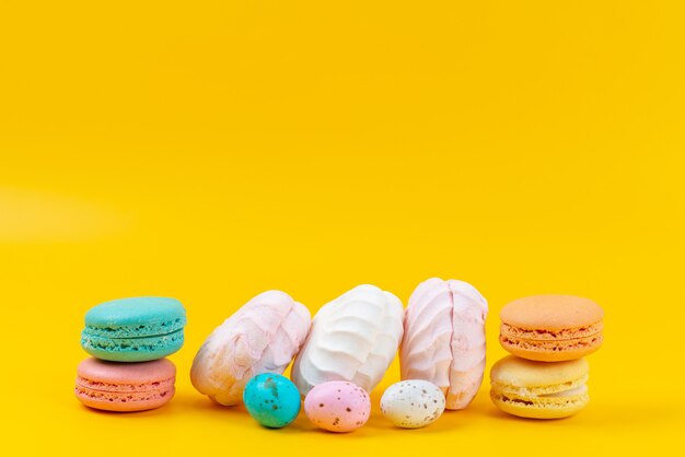 Een vooraanzicht schuimgebakjes en macarons heerlijk en zoet op geel, kleur regenboog snoep