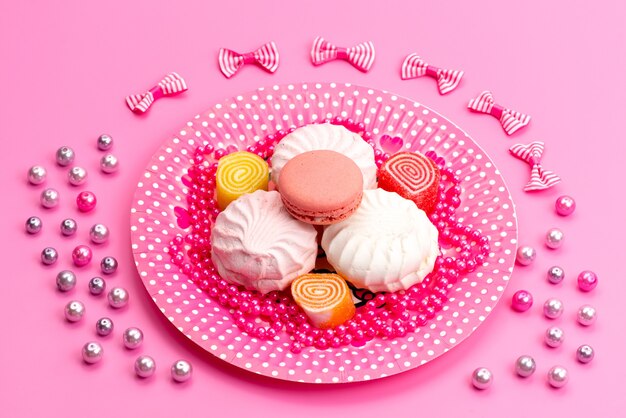 Een vooraanzicht schuimgebakjes en macarons in roze, bord samen met strikken op roze, cake biscuit banketbakkerij