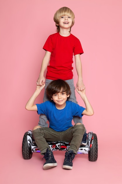 Een vooraanzicht twee jongens in rood en blauw t-shirts schattig schattig glimlachend Segway rijden op de roze vloer