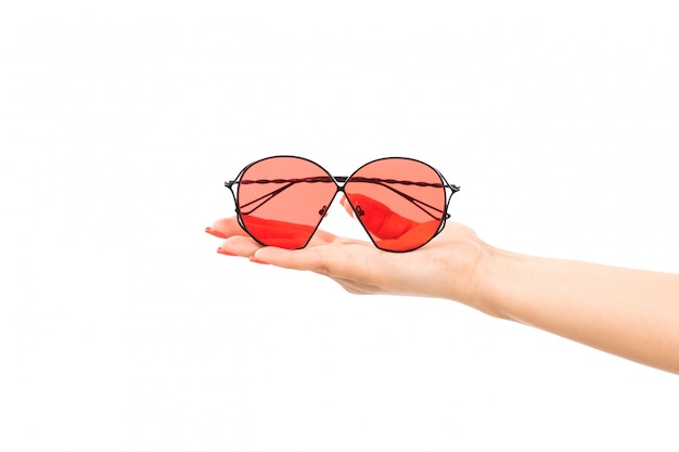Een vooraanzicht vrouwelijke hand die rode zonnebril op het wit houdt
