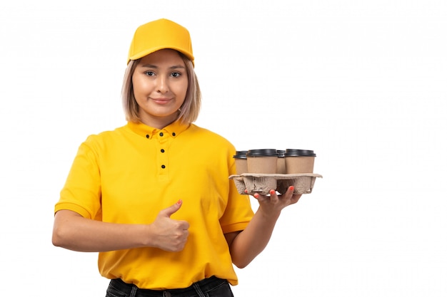 Een vooraanzicht vrouwelijke koerier in geel overhemd geel GLB en zwarte jeans die koffiekoppen op wit houden