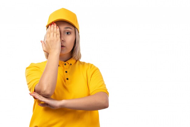 Een vooraanzicht vrouwelijke koerier in gele overhemd gele pet en zwarte jeans poseren voor haar een oog op wit